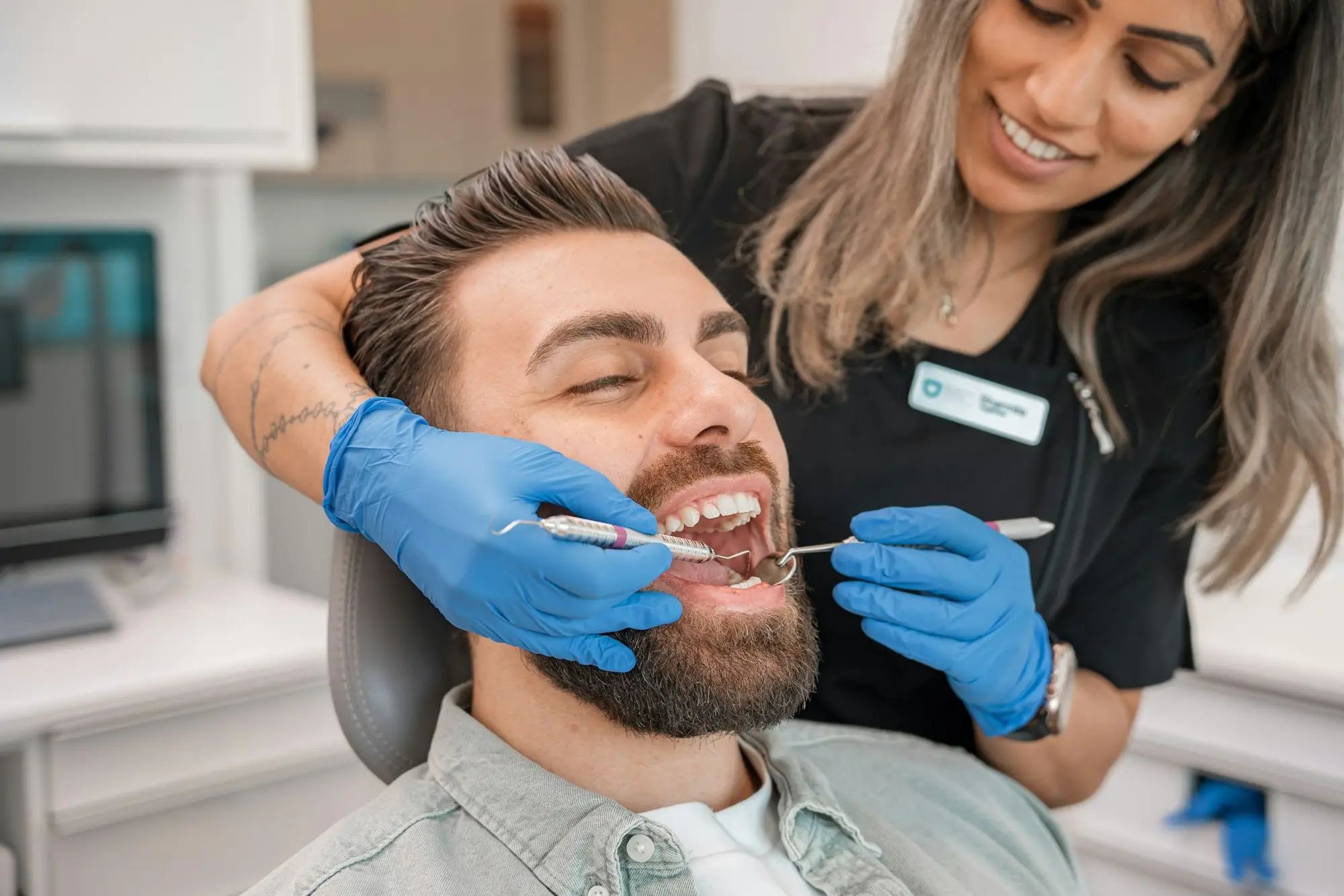 A dentist and dental assistant in blue gloves examining a patient in a bright surgery