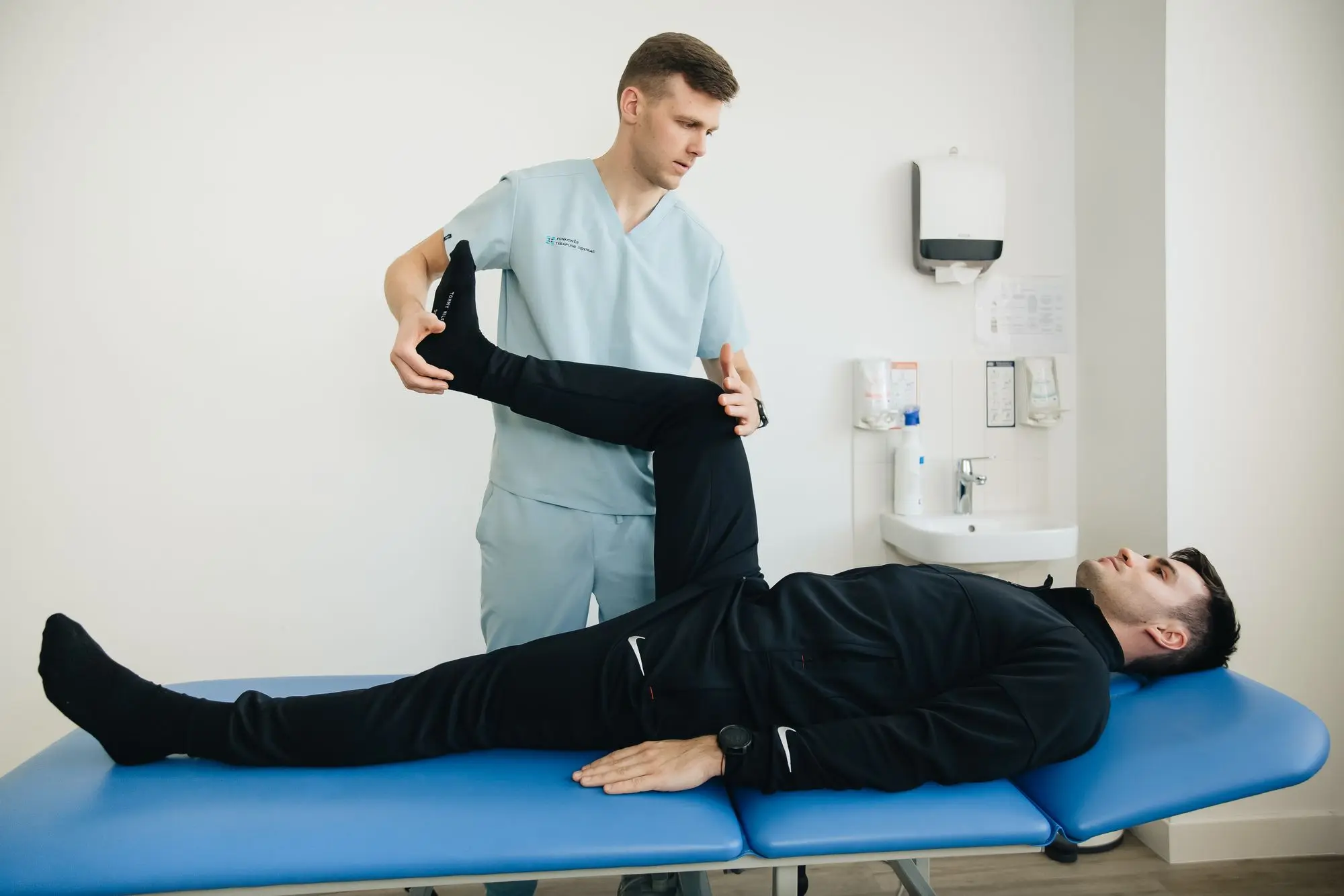 Physiotherapist stretching a patient’s leg on a blue treatment table in an allied health clinic