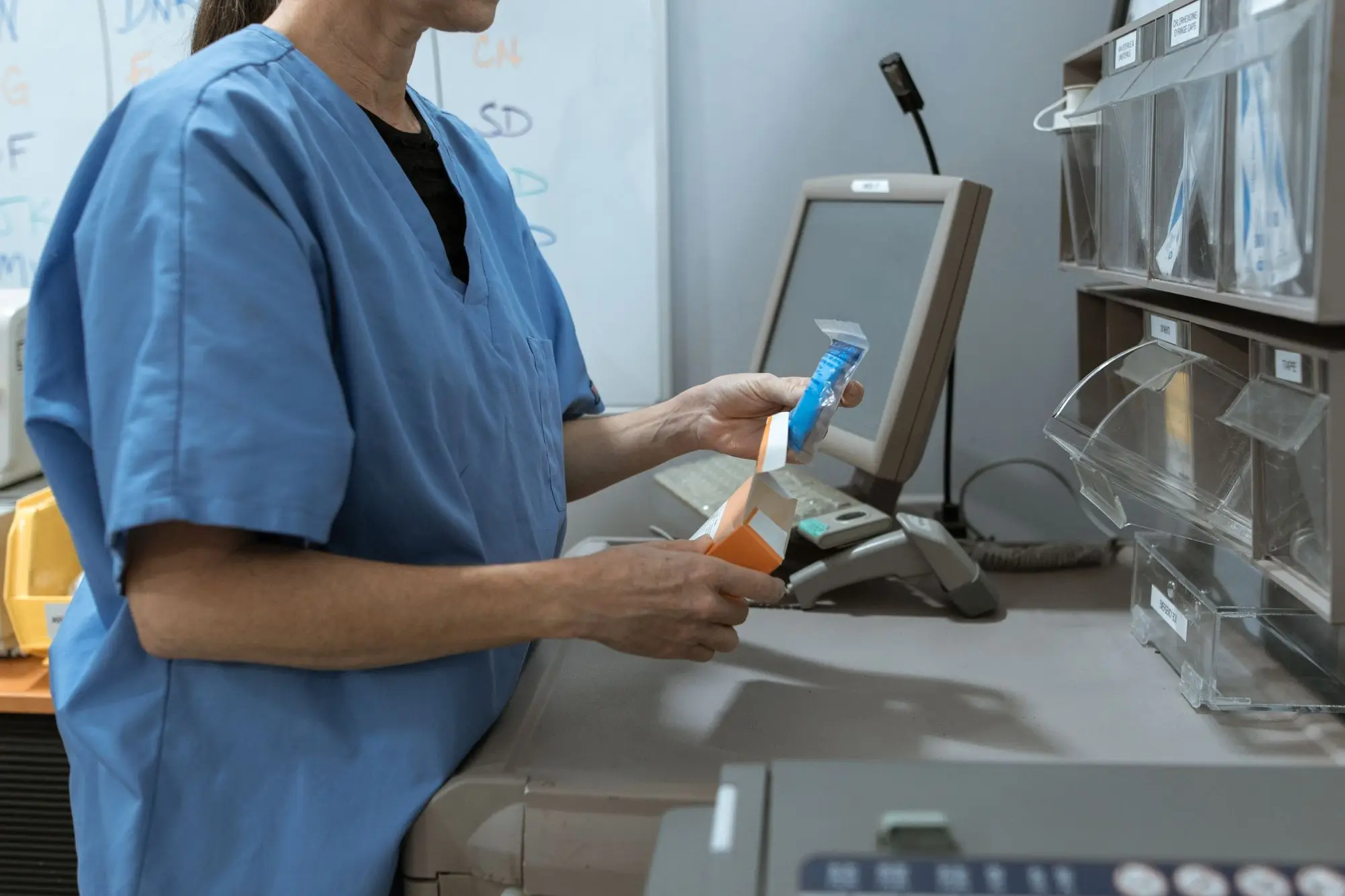 Health worker in blue scrubs scanning a medicine pack at an automated dispensing cabinet with labelled drawers